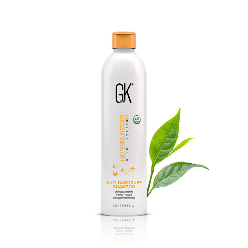 GK Hair Anti-Dandruff Shampoo 250 ml white bottle with orange cap, front view beside fresh green tea leaves