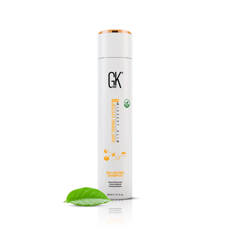 GK Hair Balancing Shampoo 300 ml bottle with a copper cap standing next to a green leaf on a white background