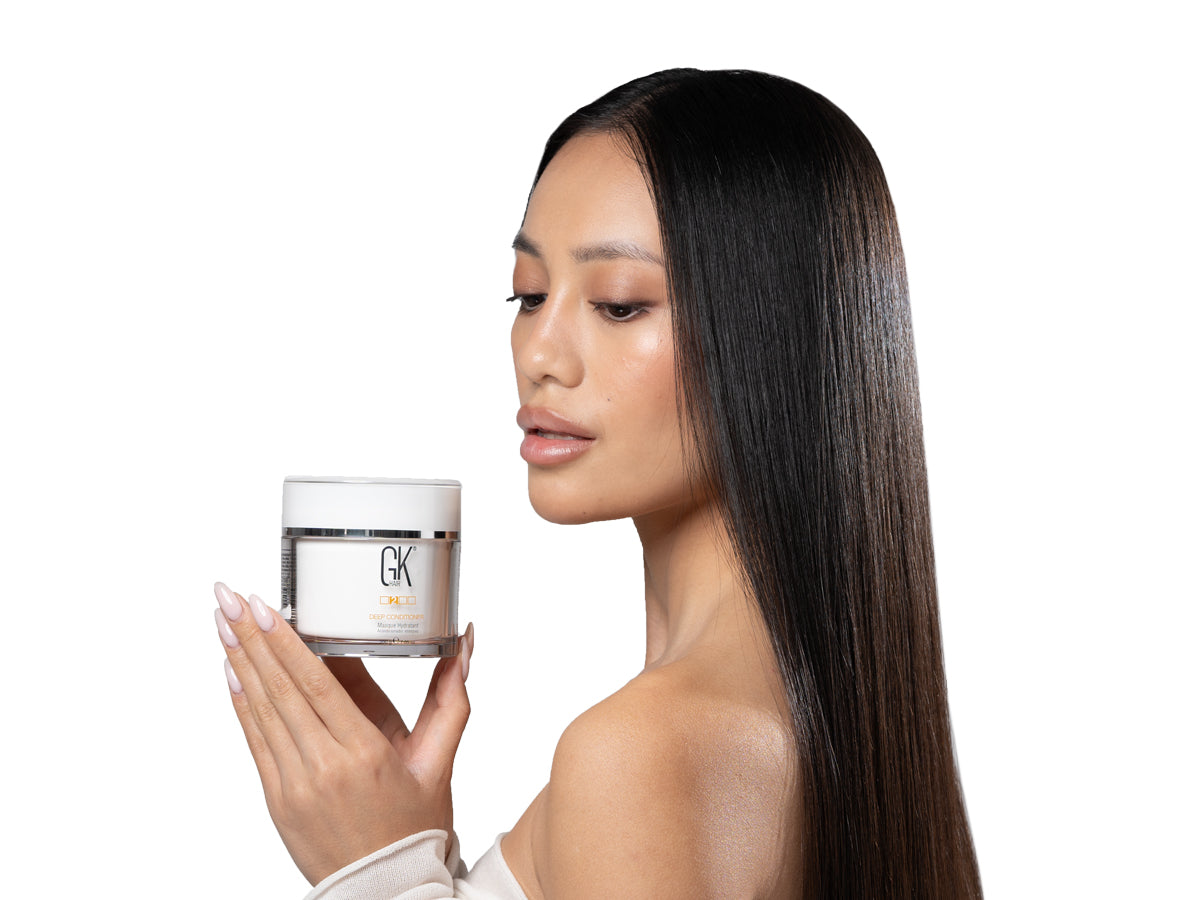A person holds a jar of GK Hair Deep Conditioner with long, sleek hair visible. The scene is minimalistic and focused on the product.