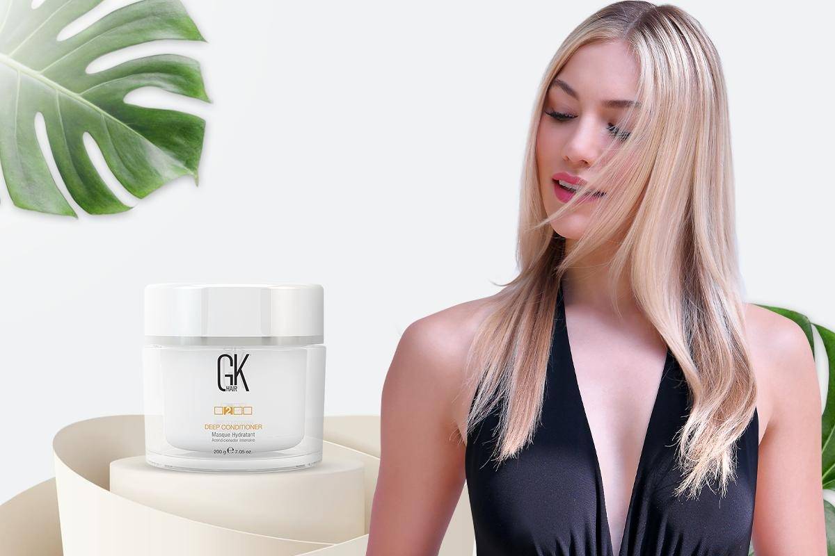 A model with long, straight hair poses next to a jar of GK hair Deep Conditioner against a minimalistic background with a leaf.